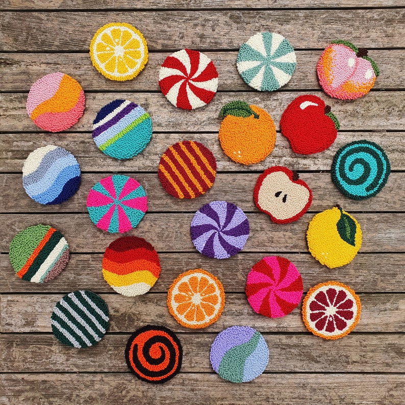May include: A collection of 20 colorful, round, embroidered coasters with various designs, including fruit, candy, and geometric patterns. The coasters are arranged on a wooden surface.