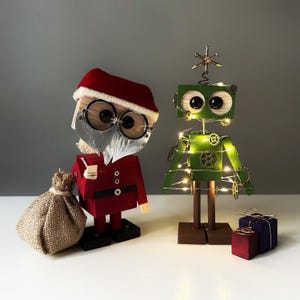May include: Wooden Christmas decorations featuring a Santa Claus figure and a robot-shaped Christmas tree. The Santa figure wears a red suit and hat, with a white beard and round glasses. The green robot tree is adorned with fairy lights and gears. A burlap sack and wrapped gifts are also present.