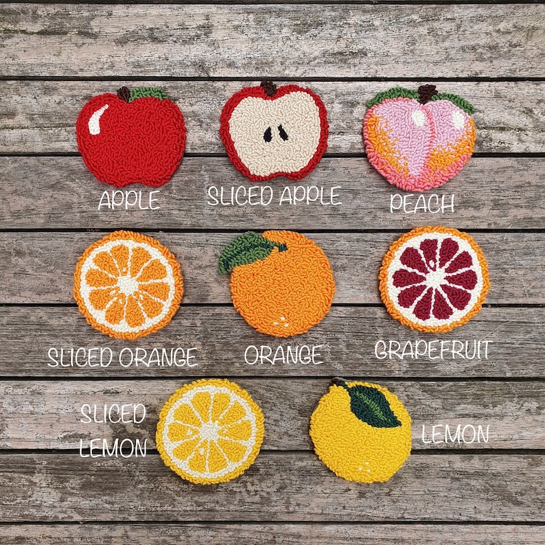 May include: Nine felt fruit coasters, including a whole apple, a sliced apple, a peach, a whole orange, a sliced orange, a grapefruit, a whole lemon, and a sliced lemon. The coasters are arranged in two rows on a wooden surface.
