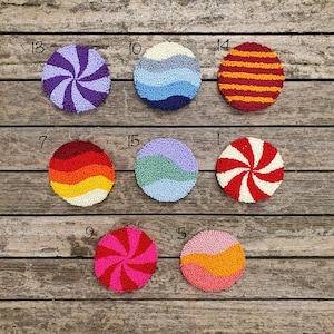 May include: Ten colorful round wall hangings with different patterns, including stripes, swirls, and waves. The hangings are made of yarn and are displayed on a wooden background.