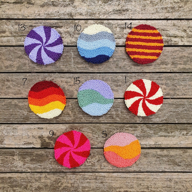 May include: Ten colorful round wall hangings with different patterns, including stripes, swirls, and waves. The hangings are made of yarn and are displayed on a wooden background.