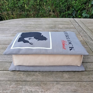 May include: A gray and beige cushion with a silhouette of Sherlock Holmes and the text "Sherlock Holmes" printed on it.
