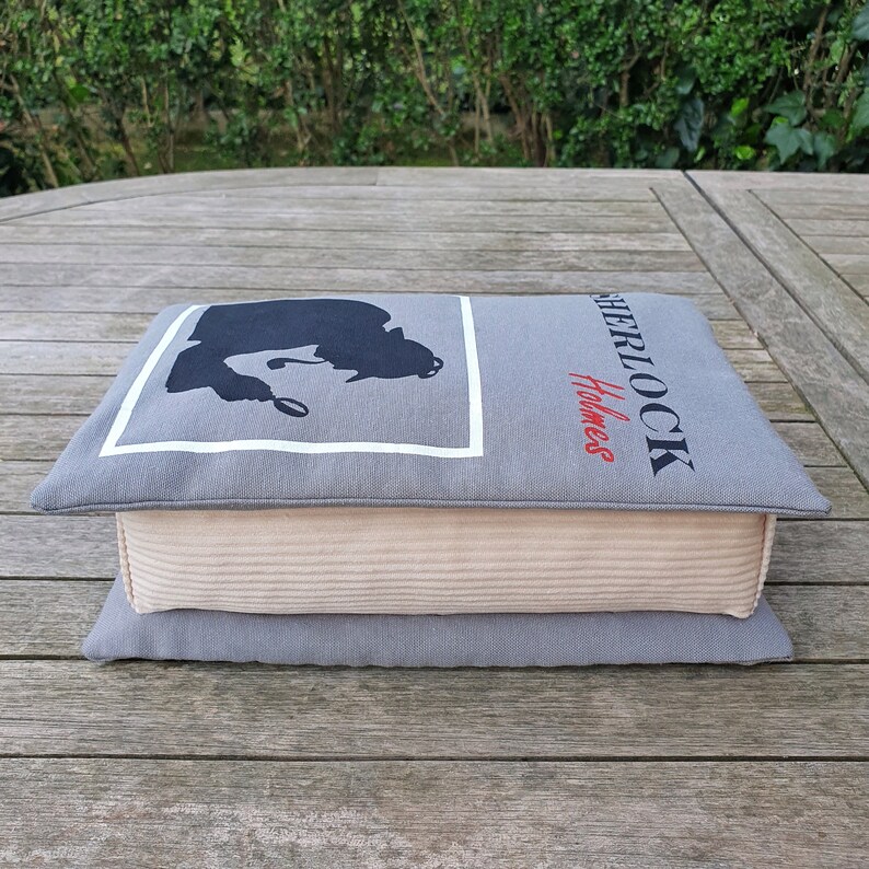 May include: A gray and beige cushion with a silhouette of Sherlock Holmes and the text "Sherlock Holmes" printed on it.