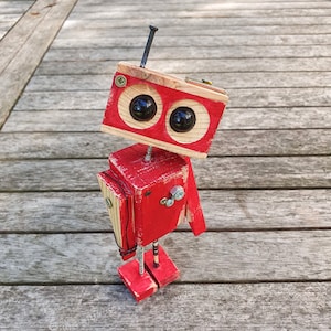 May include: A red, wooden robot with black eyes and a wooden antenna. The robot is made of recycled wood and has a rustic, handmade look.