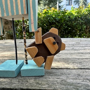 May include: A wooden toy figure with blue and white striped legs and a brown wooden bear attached to its leg with wire.