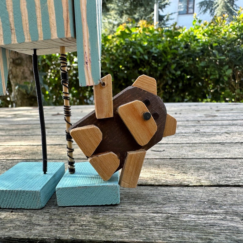 May include: A wooden toy figure with blue and white striped legs and a brown wooden bear attached to its leg with wire.