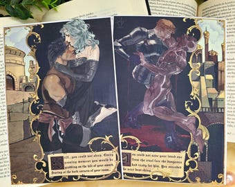 May include: Two rectangular art prints featuring fantasy illustrations with ornate gold borders. The left print shows a person with dark hair and a person with light hair in a desert setting. The right print depicts a knight in armor holding a figure.