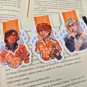 May include: Three illustrated bookmarks featuring characters in orange and white athletic jerseys with the text "PALMETTI" and numbers. The bookmarks are on a book page. Each character has a unique hairstyle and expression.