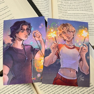 Könnte beinhalten: Zwei Kunstdrucke mit Illustrationen junger Männer mit Wunderkerzen. Ein Druck zeigt einen Mann mit dunklem Haar und einer Kreuzkette, der andere einen Mann mit blondem Haar. Beide Drucke haben einen farbenfrohen, künstlerischen Stil.