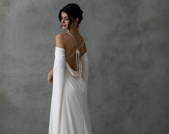 May include: A white, flowing gown with a low back and long sleeves. The gown has a cowl neck and a train.