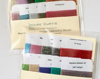 May include: A close-up of a collection of metallic embroidery threads in various colors, including amber, begonia, ruby, and twilight. The threads are organized in rows and labeled with their corresponding colors and numbers. The text "Sparkling Metallic Duo" is visible at the bottom of the image.