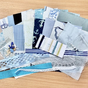 May include: A collection of blue and white fabric scraps, including gingham, stripes, and nautical prints, with a small package of embroidery floss and a few buttons. The fabric scraps are arranged in a fan shape on a wooden surface.