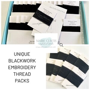 May include: A collection of black embroidery thread spools labelled "Blackwork Thread" with different sizes in a white box. The spools are arranged in rows and labelled with the size and length of the thread. The box is labelled "Maire Curtis Lakeland Studio" and "Unique embroidery & silk craft".