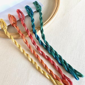 May include: Five skeins of embroidery floss in various shades of green, orange, and yellow. The floss is arranged in a rainbow pattern.