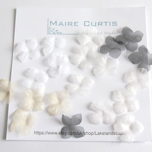 May include: Assortment of white, cream and grey fabric flower embellishments. The flowers are made of sheer fabric and have a delicate, layered look. The flowers are arranged on a white background with the text "MAIRE CURTIS Lakeland Studio" and a website address.