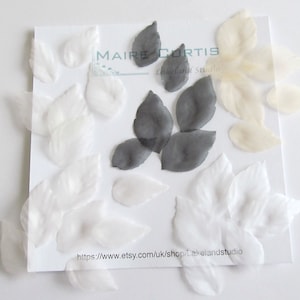 May include: Assortment of white, cream, and black fabric leaves. The leaves are made of a sheer material and are perfect for crafting projects. The image also includes the text "MAIRE CURTIS Lakeland Studio" and a website address.