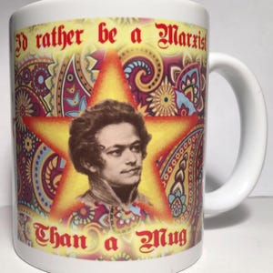 May include: White ceramic mug with a portrait of Karl Marx in a yellow star, set against a paisley pattern. The mug displays the text "I'd rather be a Marxist Than a Mug" in red and gold.