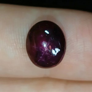 Może przedstawiać: Owalny, ciemnoczerwony kamień szlachetny o gładkiej, wypolerowanej powierzchni. Kamień ma delikatny połysk i kilka małych inkluzji.