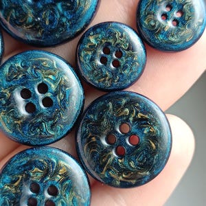 May include: A collection of round buttons featuring a deep blue and metallic gold swirling marbled pattern. Each button has a smooth, glossy finish and four central holes for attachment, showcasing a vibrant, reflective, and glittery texture.