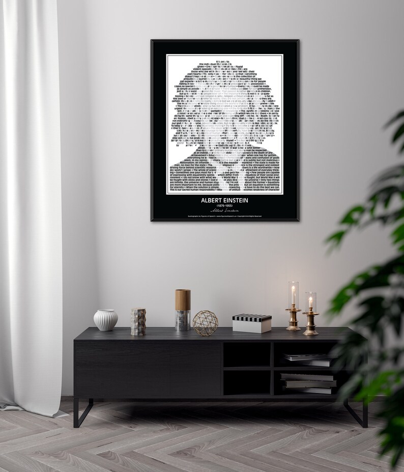 May include: A black and white typography art print featuring a portrait of Albert Einstein. The portrait is made up of words and text. The print is framed in a black frame and is hanging on a white wall. The print is above a black TV stand with a white vase, a wooden decorative object, and a black and white striped box.