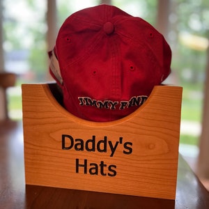 May include: A wooden hat box with the text "Daddy's Hats" engraved on the front. A red baseball cap with the text "Jimmy Fund" is inside the box.
