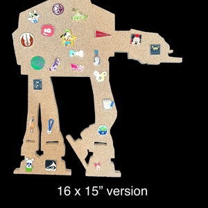 May include: A corkboard shaped like the Star Wars character AT-AT, measuring 16 x 15 inches. The corkboard is decorated with various pins and badges, including Disney characters, a lightsaber, and a bone.