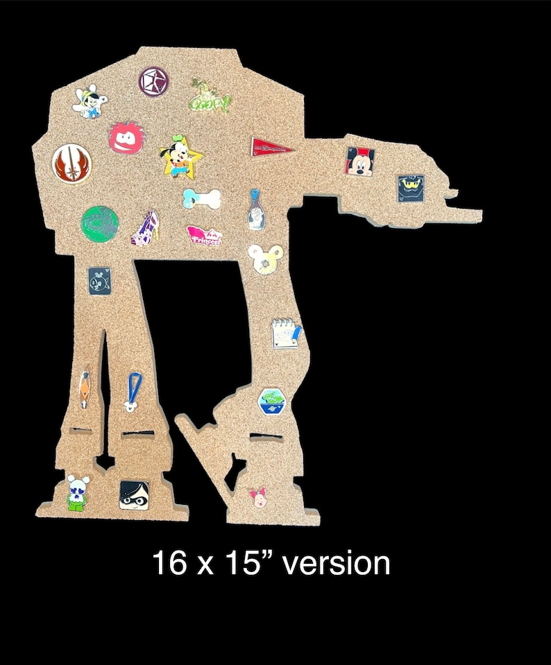 May include: A corkboard shaped like the Star Wars character AT-AT, measuring 16 x 15 inches. The corkboard is decorated with various pins and badges, including Disney characters, a lightsaber, and a bone.
