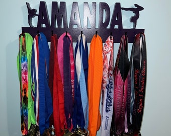 May include: A black wooden medal display rack with the name "AMANDA" in large white letters. The rack has 10 hooks for hanging medals. There are 10 colorful medals hanging on the rack.