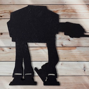 May include: Black silhouette of an AT-AT walker from Star Wars. The walker is standing on a woodgrain background.