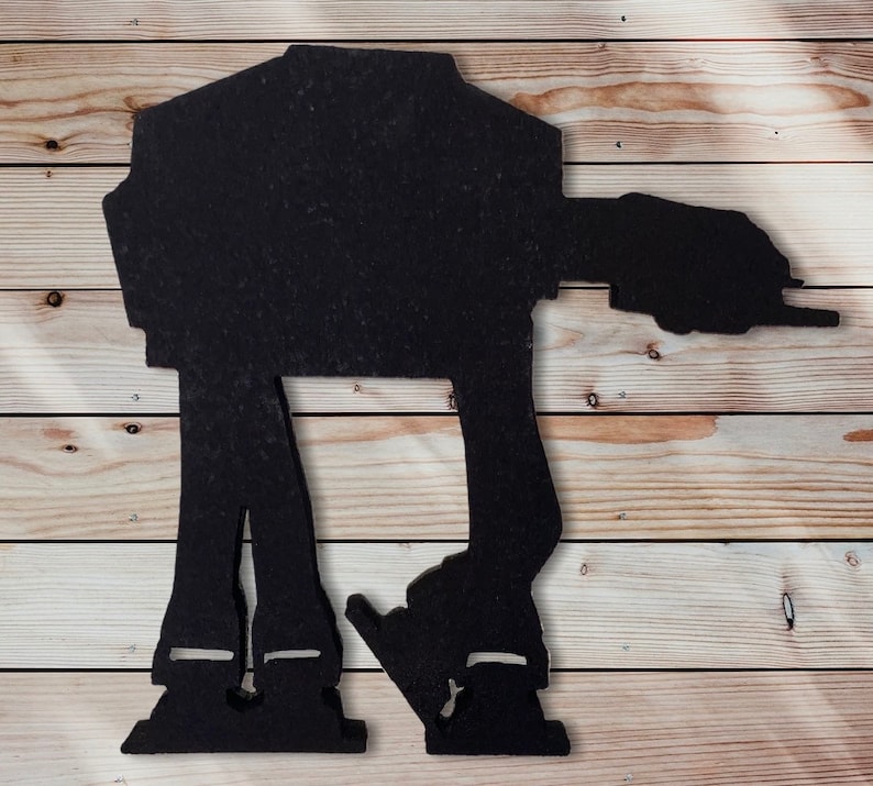 May include: Black silhouette of an AT-AT walker from Star Wars. The walker is standing on a woodgrain background.