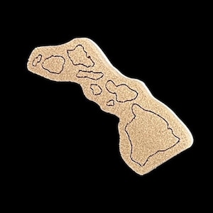May include: A tan-colored, island-shaped object with black outlines, resembling the Hawaiian Islands. The object is set against a black background, highlighting the detailed shape of the islands.