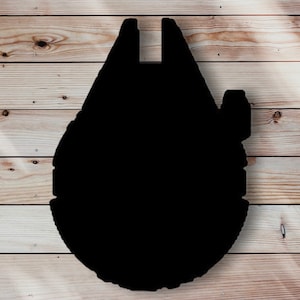 Puede incluir: Una silueta negra de la nave espacial Halcón Milenario, una nave espacial ficticia de la franquicia Star Wars. La forma distintiva de la nave es visible sobre un fondo claro de vetas de madera.