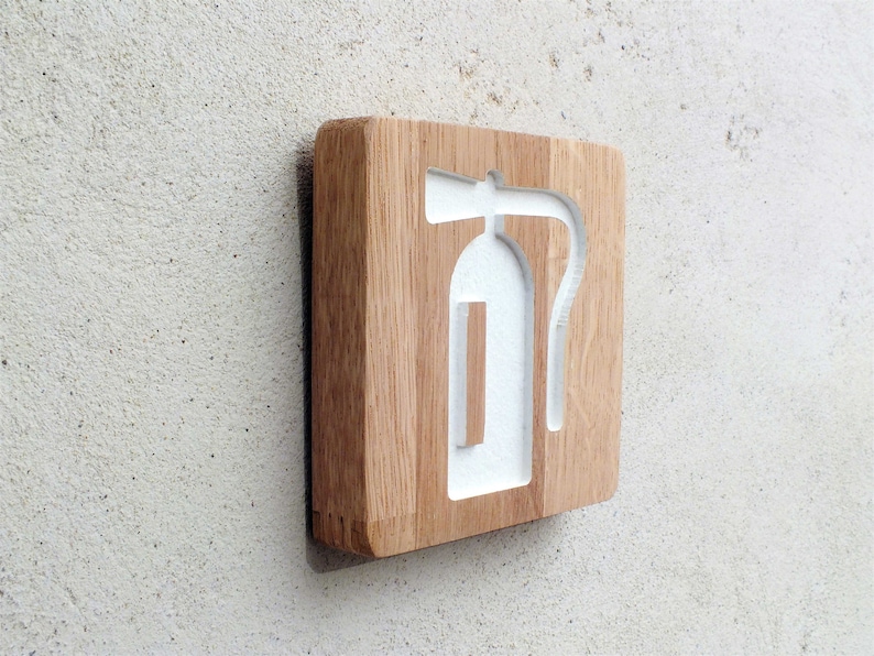 May include: A wooden sign with a white fire extinguisher symbol carved into it. The sign is mounted on a wall.