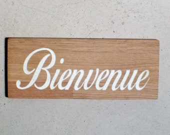 May include: A wooden sign with the word "Bienvenue" in white cursive lettering.