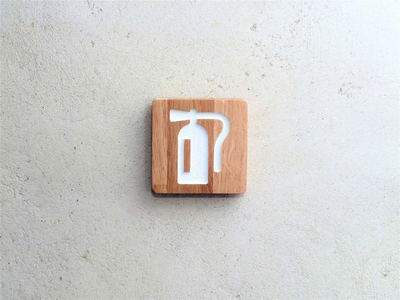 May include: A wooden sign with a white fire extinguisher symbol. The sign is made of light brown wood and has a slightly rough texture.