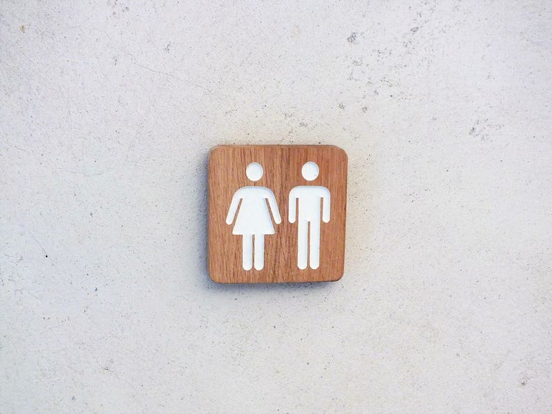 May include: A wooden sign with white painted symbols for a restroom. The sign has a light brown wood grain.
