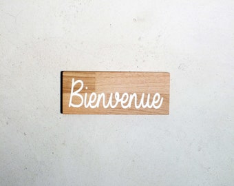 May include: A wooden sign with the word "Bienvenue" written in white cursive lettering.