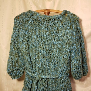 May include: A blue and green knitted sweater dress with a belt. The sweater has a loose fit and a cable knit pattern.