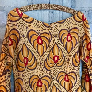 May include: A long-sleeved dress with a geometric pattern in shades of brown, yellow, and red. The dress has a zipper closure in the back.