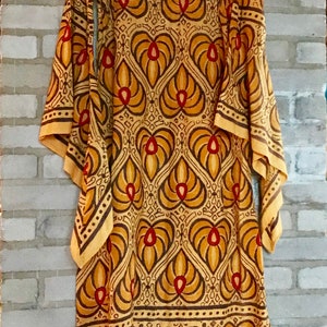 May include: A long, yellow dress with a brown and red geometric pattern. The dress has a scoop neck and long sleeves. The sleeves are wide and bell-shaped.