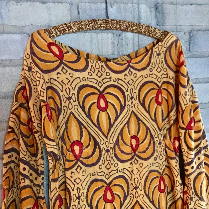May include: A long-sleeved, loose-fitting, brown and gold patterned dress with a scoop neck. The dress has a geometric pattern with red accents.