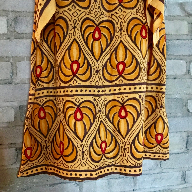 May include: A yellow and brown fabric with a repeating pattern of stylized floral motifs. The fabric has a dark brown border with small dots.