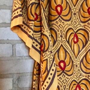 May include: A yellow fabric with a brown and red patterned design. The fabric has a geometric pattern with repeating shapes and a floral motif.