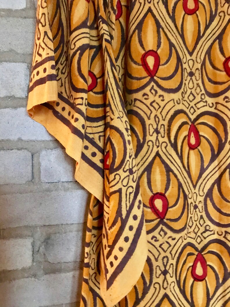 May include: A yellow fabric with a brown and red patterned design. The fabric has a geometric pattern with repeating shapes and a floral motif.