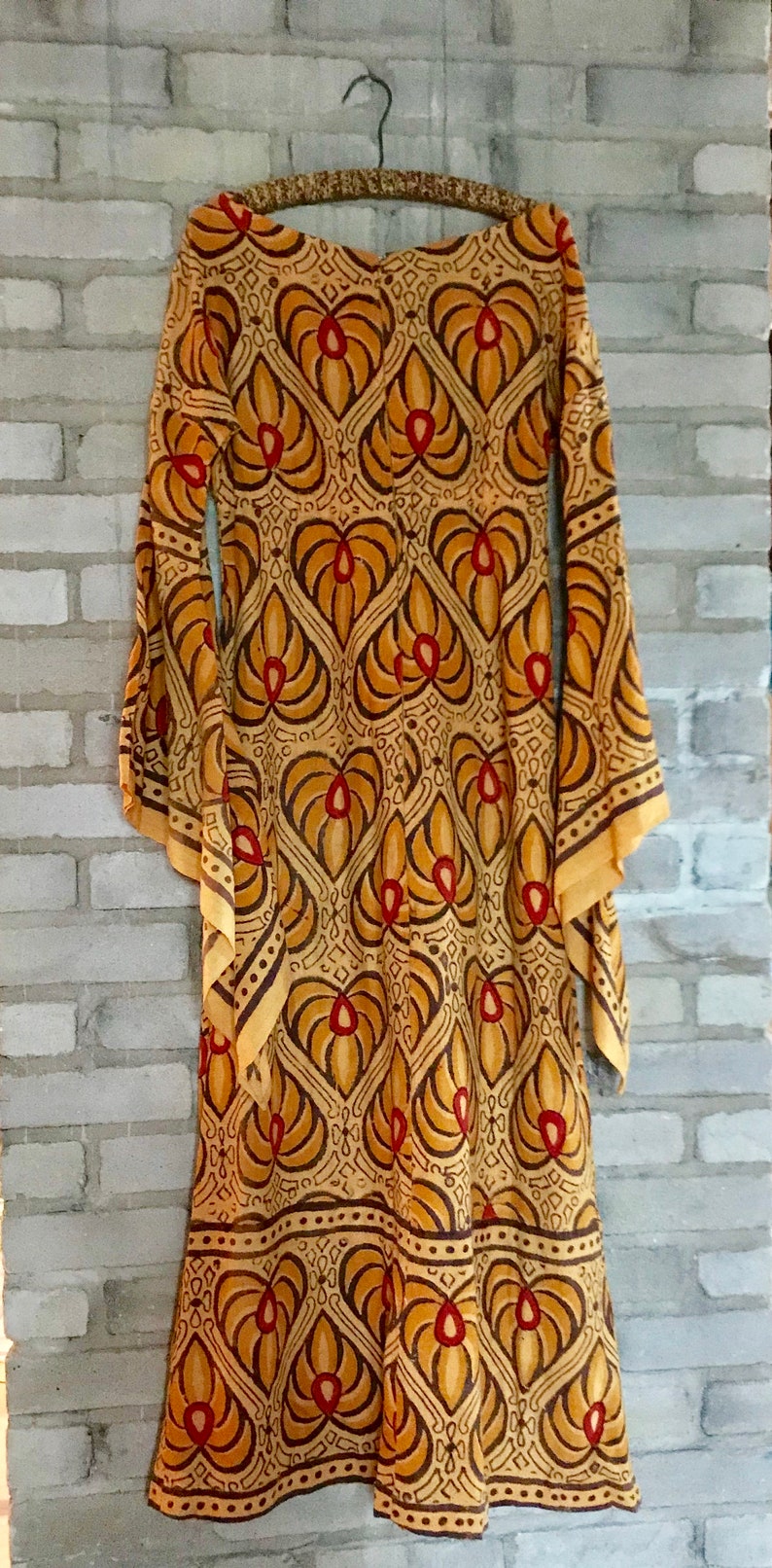 May include: A long, flowing dress with a brown and orange geometric pattern. The dress has a scoop neck and long sleeves. The fabric is sheer and has a vintage feel.