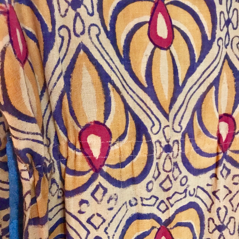 May include: Close-up of a fabric with a repeating pattern of stylized flowers in shades of yellow, blue, and red. The fabric has a textured surface and appears to be woven.