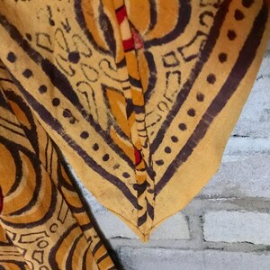 May include: Close-up of the seam of a yellow and brown fabric with a geometric pattern. The fabric is folded over and the seam is visible.