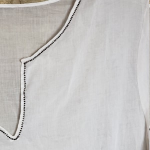 May include: White cotton top with a V-neckline and black beaded trim.