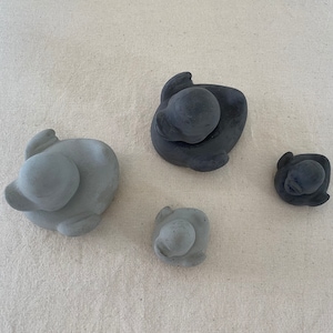 Może przedstawiać: Cztery małe ceramiczne figurki kaczek. Dwie są szare, a dwie czarne. Kaczki siedzą wszystkie w pozycji siedzącej z pochyloną głową.