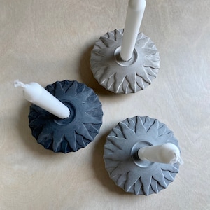 Könnte beinhalten: Drei Kerzenhalter aus Beton mit einem Sonnenstrahlen-Design. Jeder Halter hat eine weiße Kerze in der Mitte.